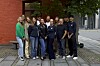 Gruppe mennesker poserer på fortauet foran en rød murbygning.