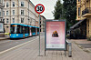 Blå trikk passerer et reklameskilt på et fortau i en bygate.